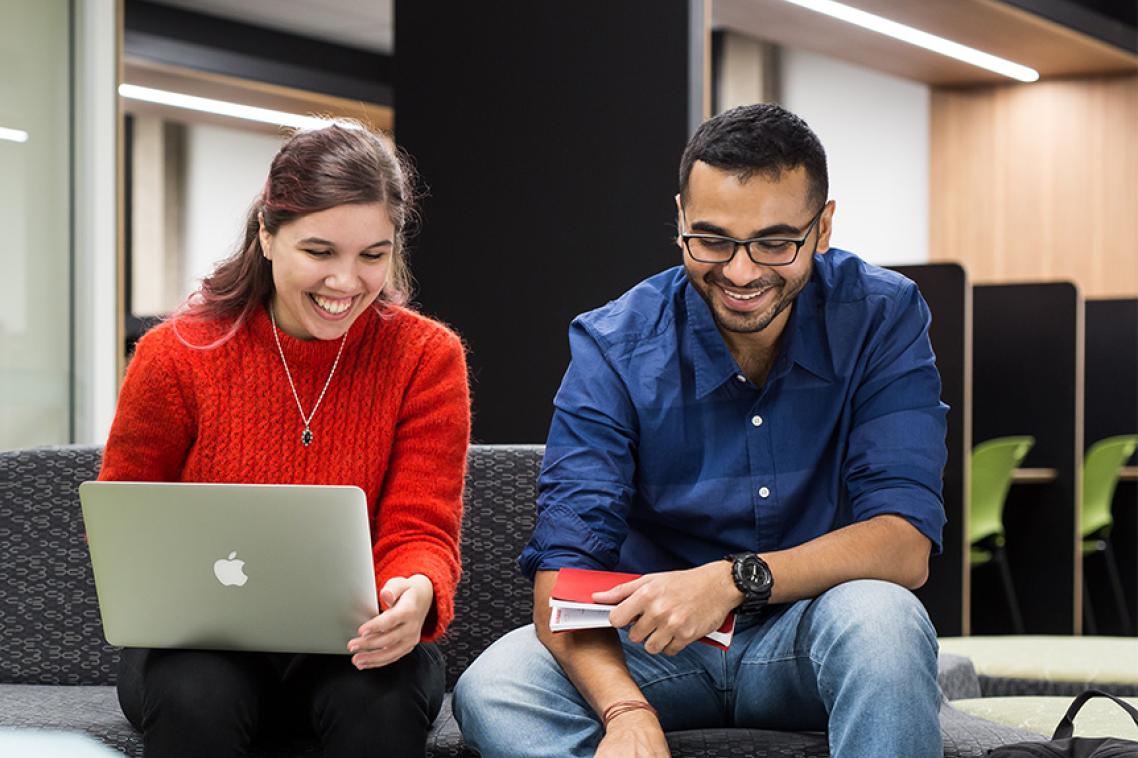 Two students studying together using a laptop and notebooks.